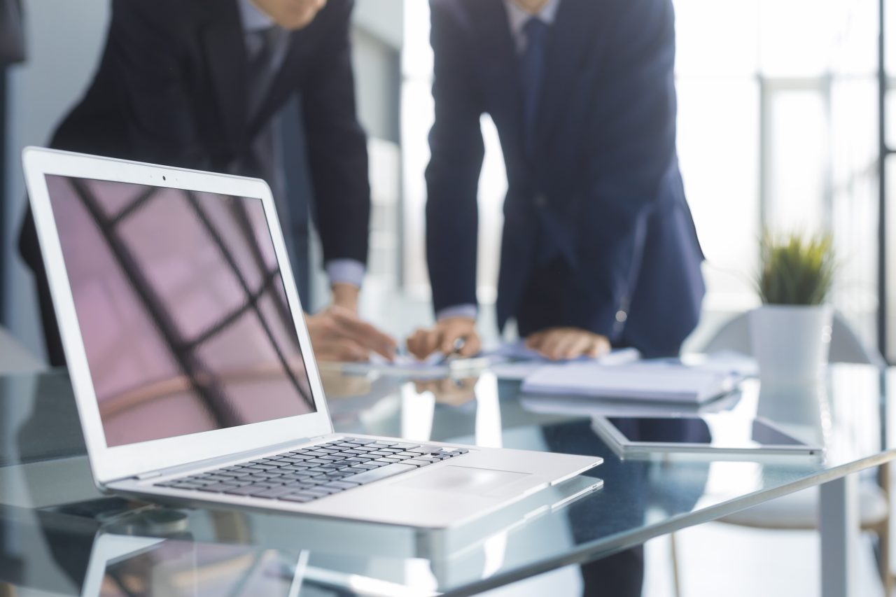 business professionals working together office desk analyzing financial statistics displayed laptop screen