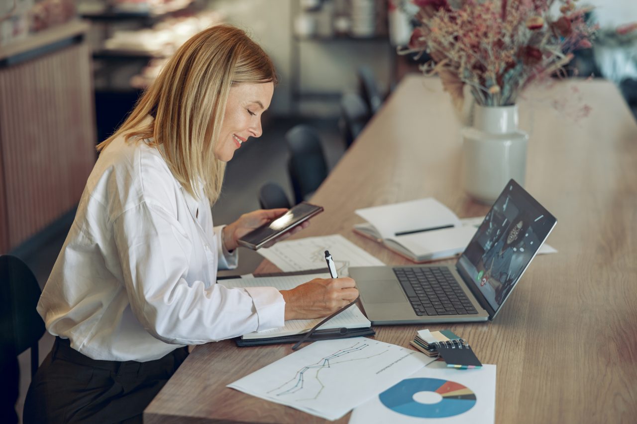 smiling business woman working laptop making notes cozy coworkign space interior
